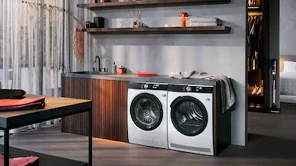 Wasmachines staan naast een houten kast met een wasbak en een plank. Er staat ook een houten tafel.