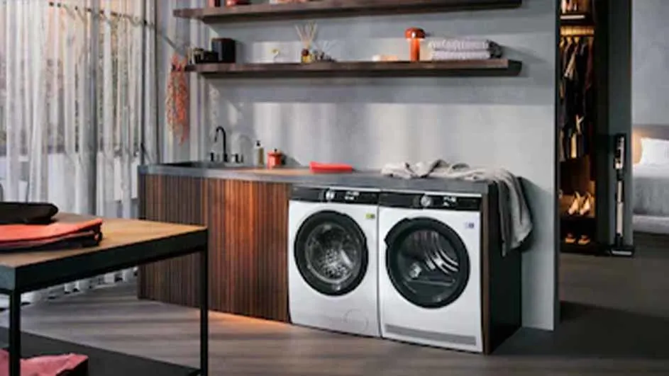 Wasmachines staan naast een houten kast met een wasbak en een plank. Er staat ook een houten tafel.