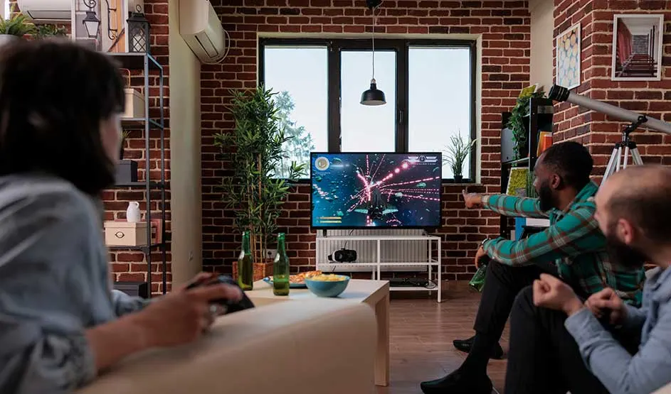 Vrienden zitten samen in een bakstenen woonkamer en kijken naar een tv met kleurrijke beelden.