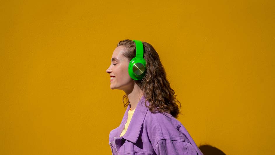 Profiel van een vrouw met een paarse jas en groene koptelefoon tegen een gele achtergrond.