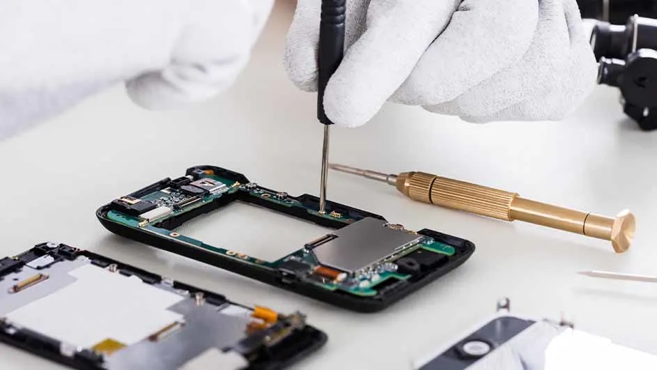 Een persoon met witte handschoenen repareert een telefoon met zwart gereedschap op een witte tafel.