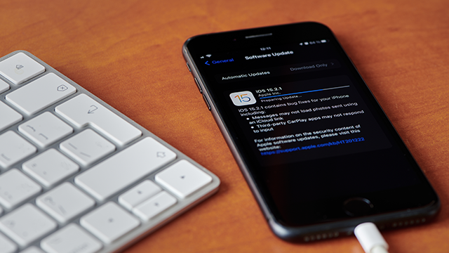 Toetsenbord links, een zwarte iPhone rechts met software-update iOS 15.2.1 op een houten tafel.