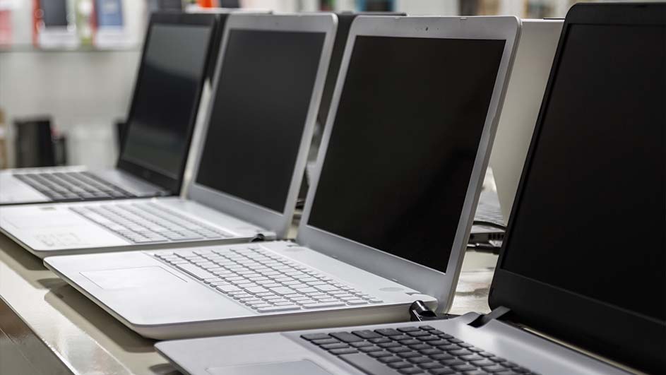 Rij laptops met zilveren behuizing en zwarte schermen staan op een rij op een tafel. De achtergrond is wazig.