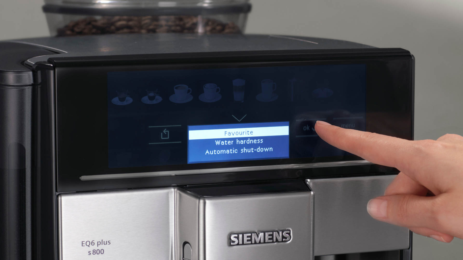 Een Siemens EQ6 koffiemachine met een aanraakscherm waarop 'Water hardness' geselecteerd is. Een vinger wijst naar 'ok'.
