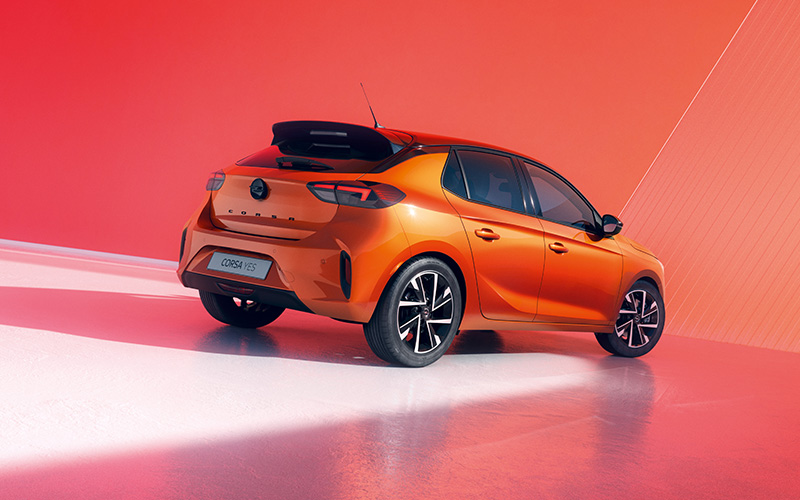 Oranje Opel Corsa Electric, achteraanzicht, gepresenteerd tegen een rode achtergrond.