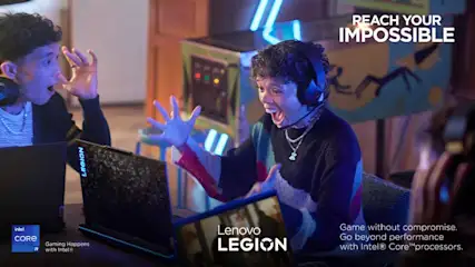 Twee gamers, met koptelefoons, vieren een overwinning voor een Lenovo Legion-laptop in een kamer met arcade-elementen.