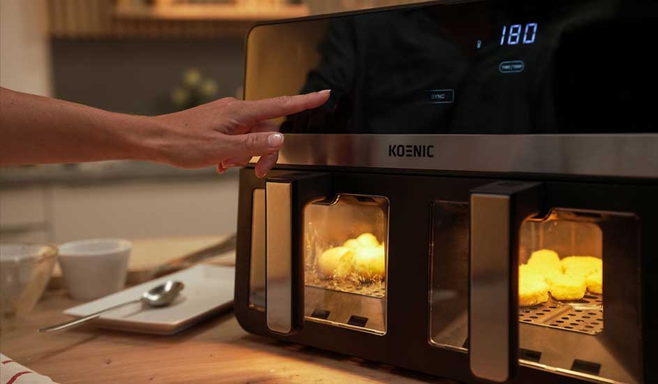 Zwarte Koenic airfryer met twee lades, digitaal display en verlichte binnenkant. Kipnuggets worden bereid. Merk: Koenic.