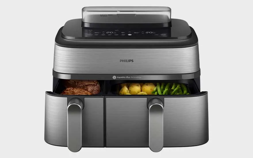 Black Koenic air fryer with two drawers, digital display and illuminated interior. Chicken nuggets are being prepared. Brand: Koenic.