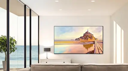Een woonkamer met een groot raam met uitzicht op zee, een schilderij van Mont Saint-Michel en een grijze bank.