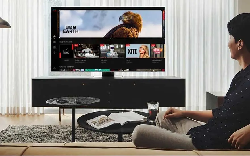 A man relaxes on the couch in a modern living room and browses the smart TV menu, with BBC Earth visible on screen.