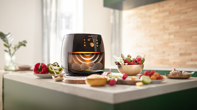 Een zwarte airfryer staat op een aanrecht met groenten en fruit, klaar om te koken.