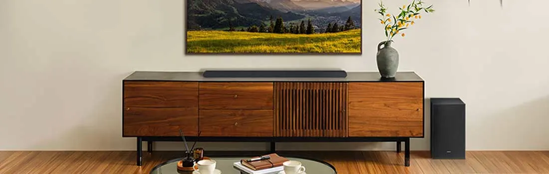Moderne woonkamer met tv boven houten dressoir, soundbar, subwoofer, planten en berglandschap op het scherm.