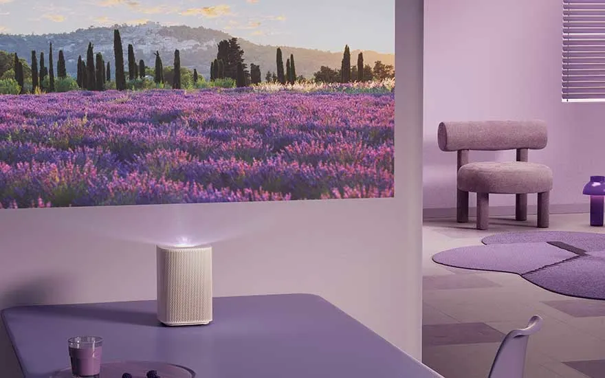 In een paars ingerichte kamer projecteert een compacte projector een lavendelveld met heuvels en bomen op de muur.