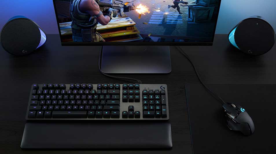 Donkere gaming opstelling met groot scherm, RGB toetsenbord, muis en krachtige luidsprekers, terwijl een actiespel vol explosies wordt gespeeld.