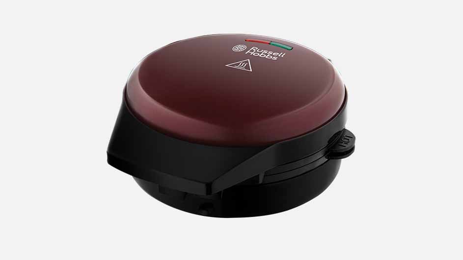 Een ronde, bordeauxrode en zwarte Russell Hobbs wafelmaker staat op een witte achtergrond.