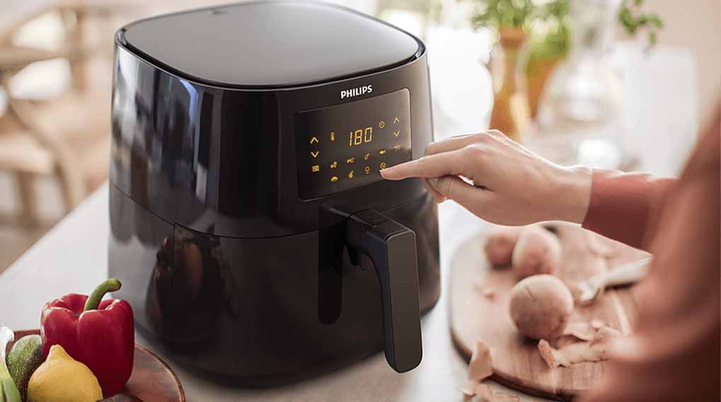 Een zwarte Philips airfryer met een digitaal display waarop 180 graden staat, een hand en groenten.