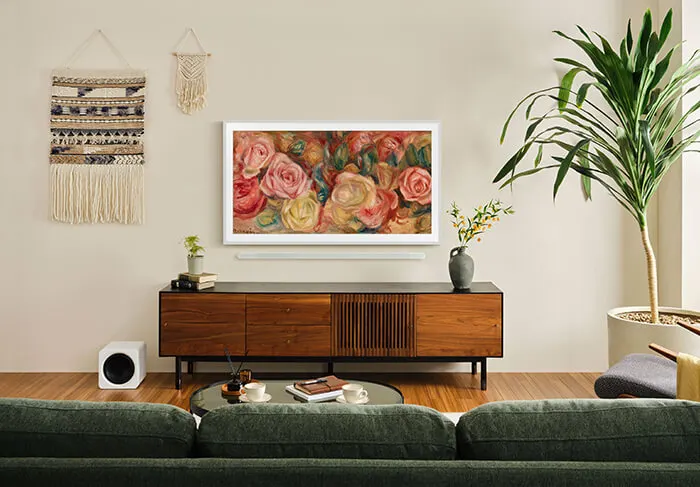 Een woonkamer met een groene bank, houten dressoir en een tv met bloemenkunst aan de muur.