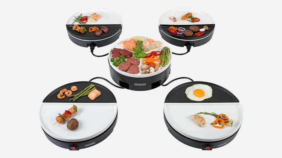 Vier kleine, zwart-witte raclette-grills zijn aangesloten op een centrale schaal met vlees, vis en groenten.