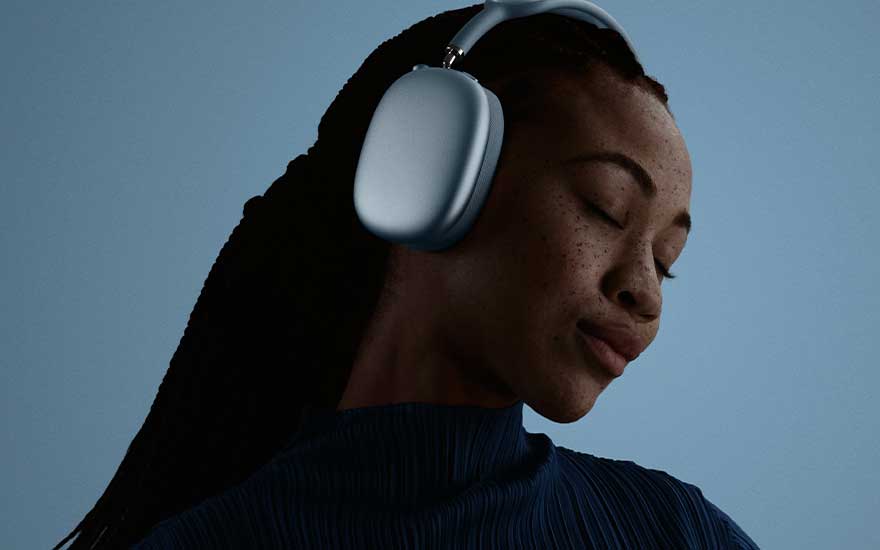 A person wearing light blue over-ear headphones tilts their head with eyes closed against a dark blue backdrop, absorbed in sound.