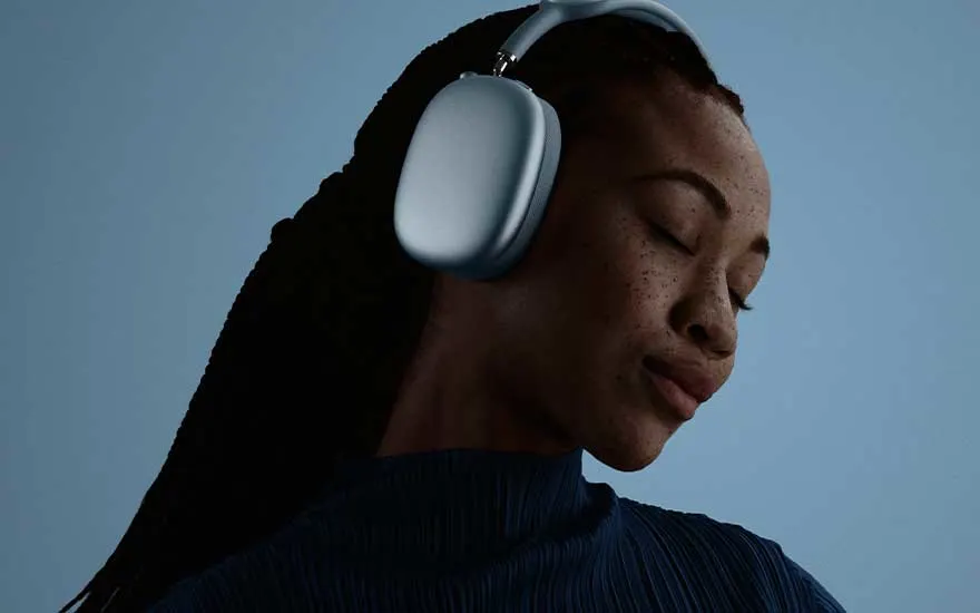 A person wearing light blue over-ear headphones tilts their head with eyes closed against a dark blue backdrop, absorbed in sound.