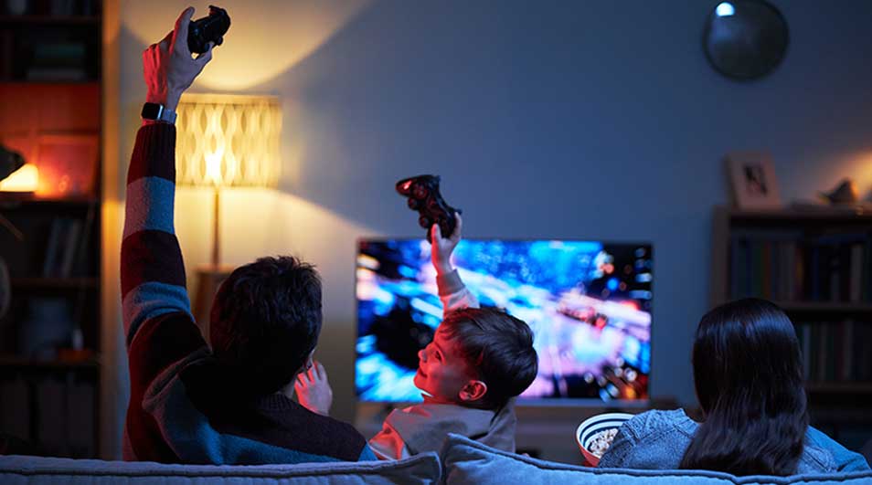 Een gezin zit op de bank en speelt of kijkt enthousiast naar een videogame op tv in een gezellige kamer.