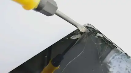 A screwdriver is used to remove the cracked screen of a tablet or smartphone. No brand is visible.