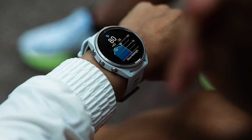Een sporter controleert zijn slaapgegevens op een Garmin smartwatch tijdens het dragen van een witte sportjas.