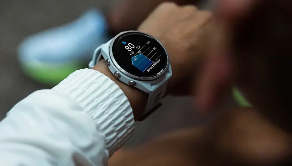 Een sporter controleert zijn slaapgegevens op een Garmin smartwatch tijdens het dragen van een witte sportjas.