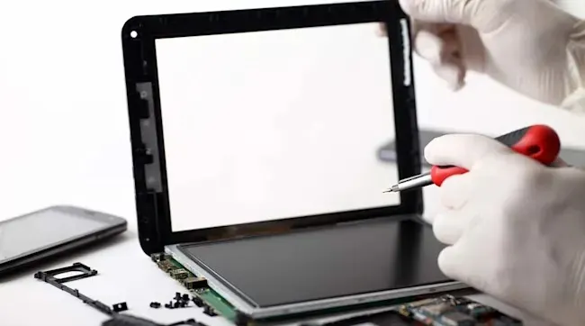 Een persoon met handschoenen repareert een tablet met een rode schroevendraaier, onderdelen en een smartphone op een witte ondergrond.