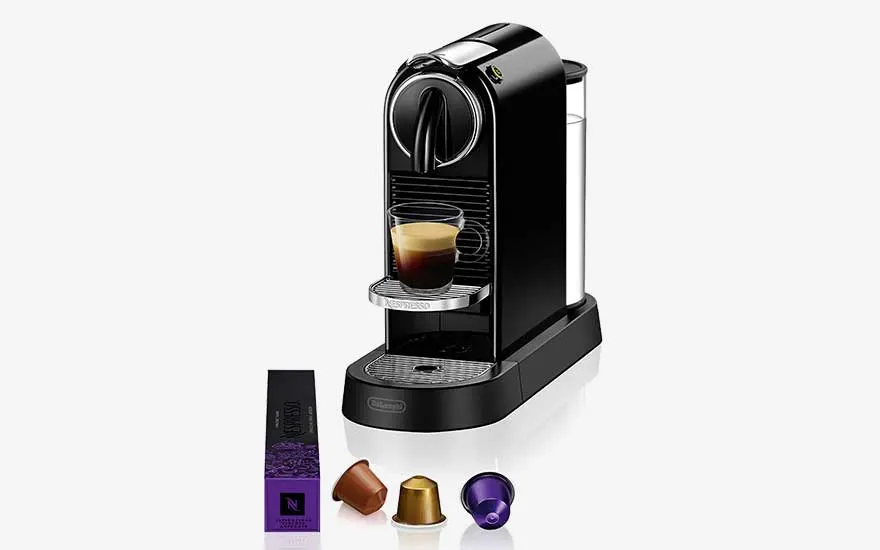 Een zwarte espressomachine met een vers kopje koffie staat op een witte achtergrond, met capsules en een doos ervoor.