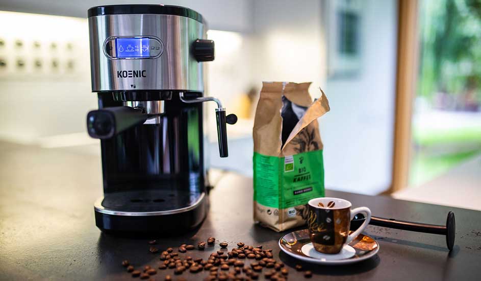 Op het aanrecht staat een Koenic espressomachine met een zak koffiebonen, een espressokopje en losse koffiebonen eromheen.
