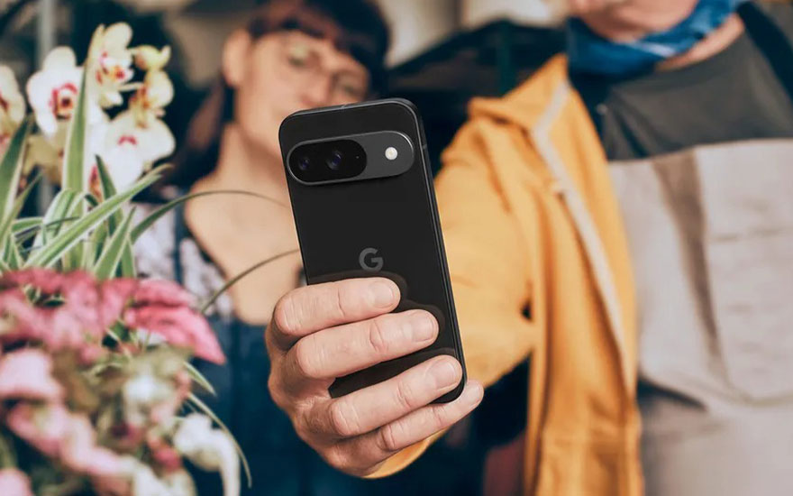Zwarte Google Pixel smartphone wordt vastgehouden met bloemen op achtergrond. Persoon in gele jas toont het elegante camera-eiland design.