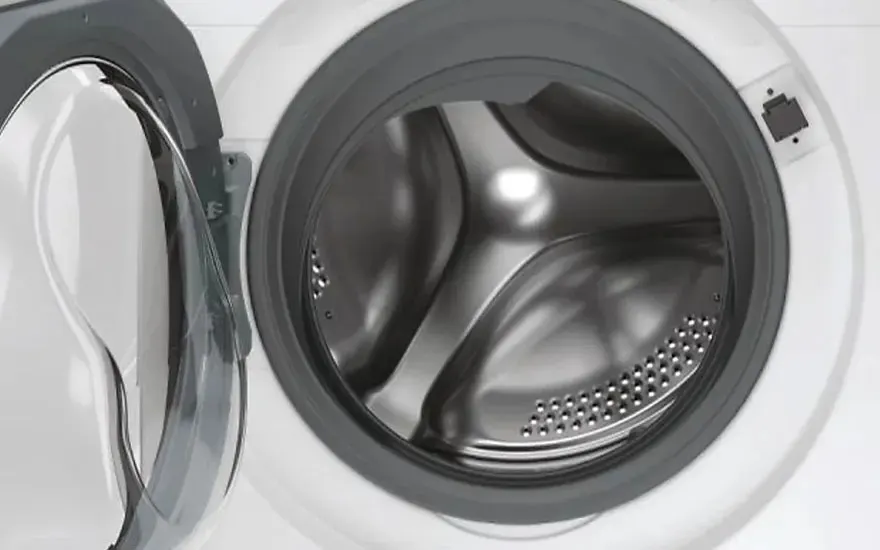 Een close-up van een geopende wasmachine met de deur aan de linkerkant. De binnenkant toont een glanzende roestvrijstalen trommel met kleine gaatjes aan de onderkant. De machine heeft een witte buitenkant met een grijze rubberen afdichting.