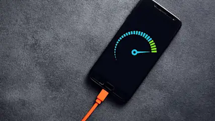 Een telefoon met een laadscherm ligt op een grijze ondergrond, verbonden met een oranje oplaadkabel.