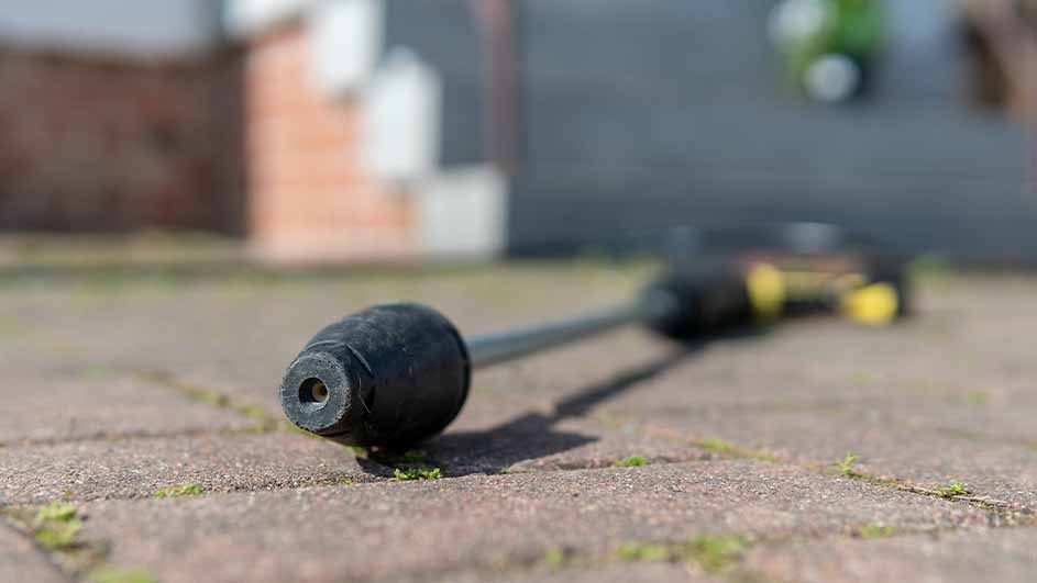 Close-up van een hogedrukreinigerlans die op een terras van bakstenen ligt; de achtergrond is onscherp.