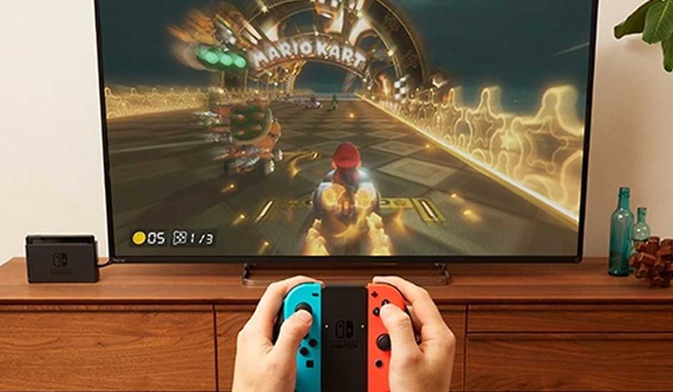 Iemand speelt Mario Kart op een Nintendo Switch met rode en blauwe Joy-Con, aangesloten op een tv in een woonkamer.