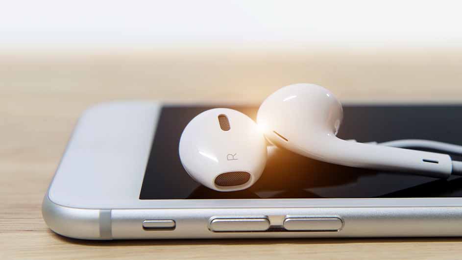 Witte oortjes liggen op een zilverkleurige smartphone met zwart scherm, op een houten oppervlak.