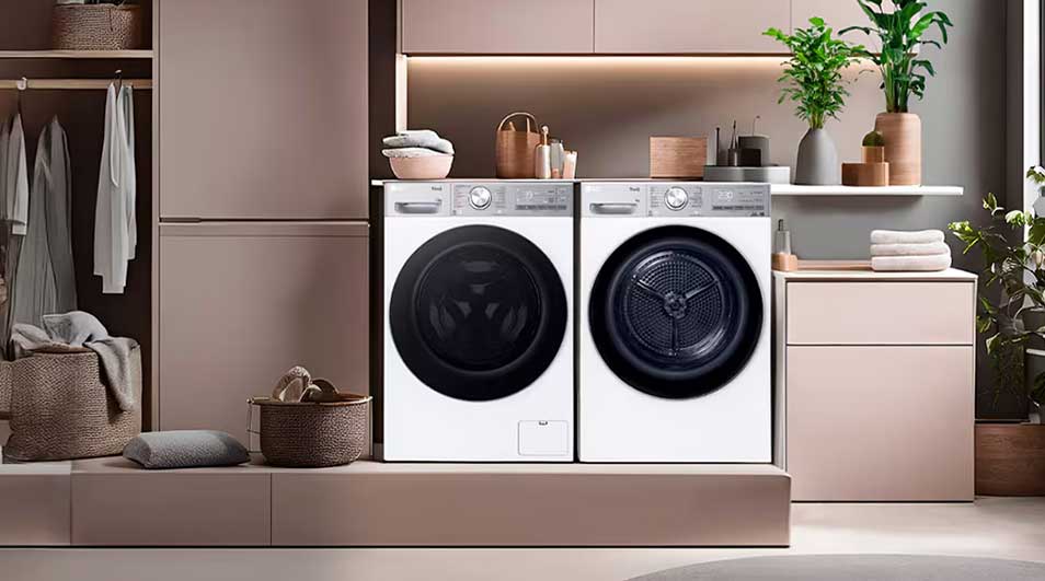 Moderne wasruimte met wasmachine en droger, zachte roze kasten, open garderobe, manden, handdoeken en groene planten.
