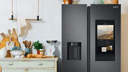 Keuken met een grijze Samsung koelkast met scherm, en houten keukengerei op een groen kastje.