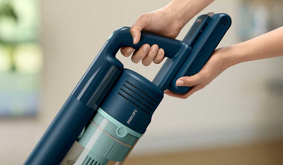 Two hands swap the battery on a slim blue Philips cordless vacuum cleaner, keeping the device ready for uninterrupted home cleaning.