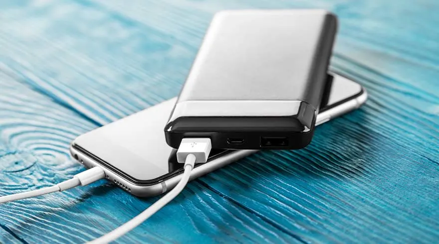 Een zilveren smartphone en een zwarte powerbank liggen op een blauwe houten ondergrond en zijn met een witte kabel verbonden.