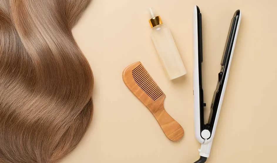 Wavy, glossy hair lies beside a comb, a spray bottle and a hair straightener on a soft beige surface.