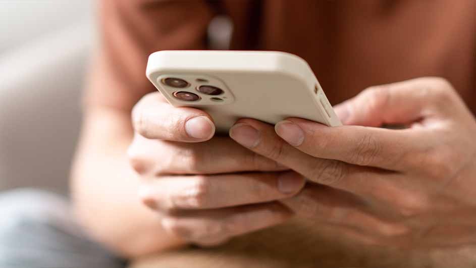 A person holds a white phone with a triple-lens camera in both hands, wearing a tan shirt.