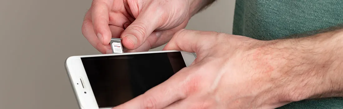 Een hand plaatst een simkaart in een witte smartphone. De achtergrond is effen grijs.