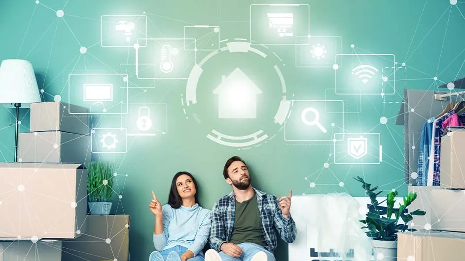 Een stel zit tussen verhuisdozen, wijzend naar digitale iconen op een blauwgroene muur. Een lamp en plant staan op dozen.