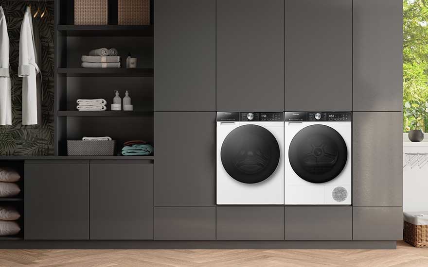 Zwarte en witte wasmachine en droger ingebouwd in een moderne, donkere kast met open schappen en uitzicht op groen buiten