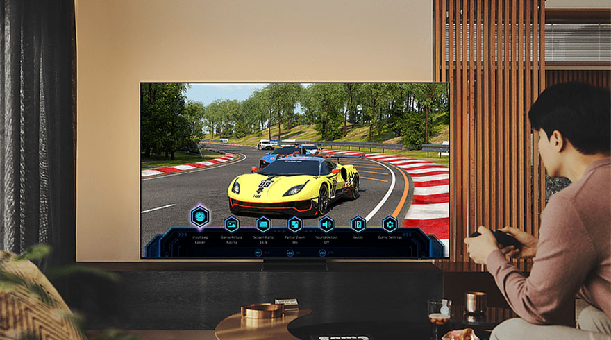 Een man speelt een racegame op een grote tv. De auto is geel en rijdt op een circuit met bomen op de achtergrond.