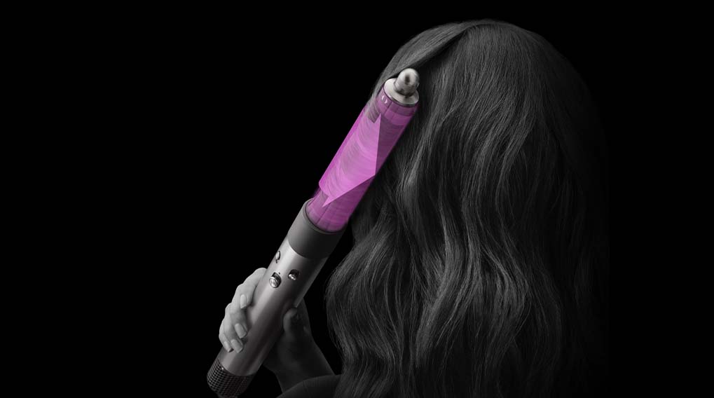 Een persoon gebruikt een paarse styler op golvend haar tegen een zwarte achtergrond.