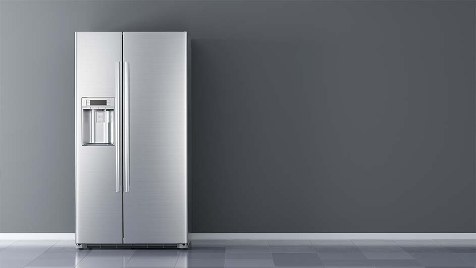 A stainless steel refrigerator with dispenser stands against a gray wall and floor.