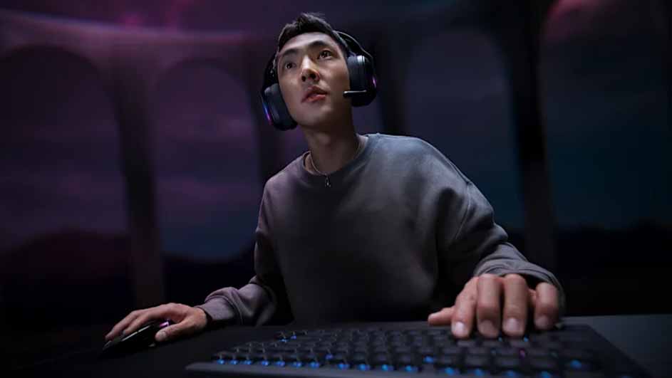 Man geconcentreerd tijdens het gamen, met een Logitech G-headset en een toetsenbord en muis in een donkere kamer met paarse verlichting.